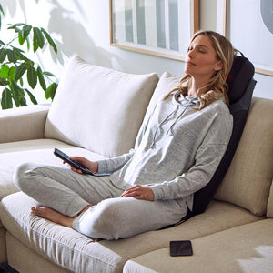 Woman on couch sits back and relaxes while enjoying a massage from the Homedics 2-in-1 Shiatsu Massage Cushion and Cordless Body Massager