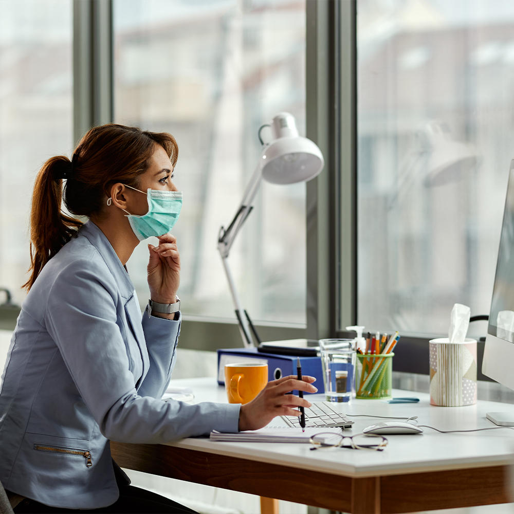 Woman sits at work desk while wearing a Homedics Single Use Ear-Loop Face Mask (10 Count)