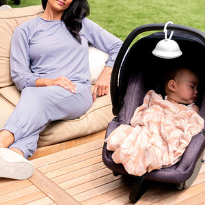 Woman relaxes as baby in baby carrier sleeps with Homedics SoundSpa On-The-Go attached