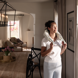 Woman standing looking out the window while enjoying her Homedics Shiatsu Rechargeable Neck Massager with Heat