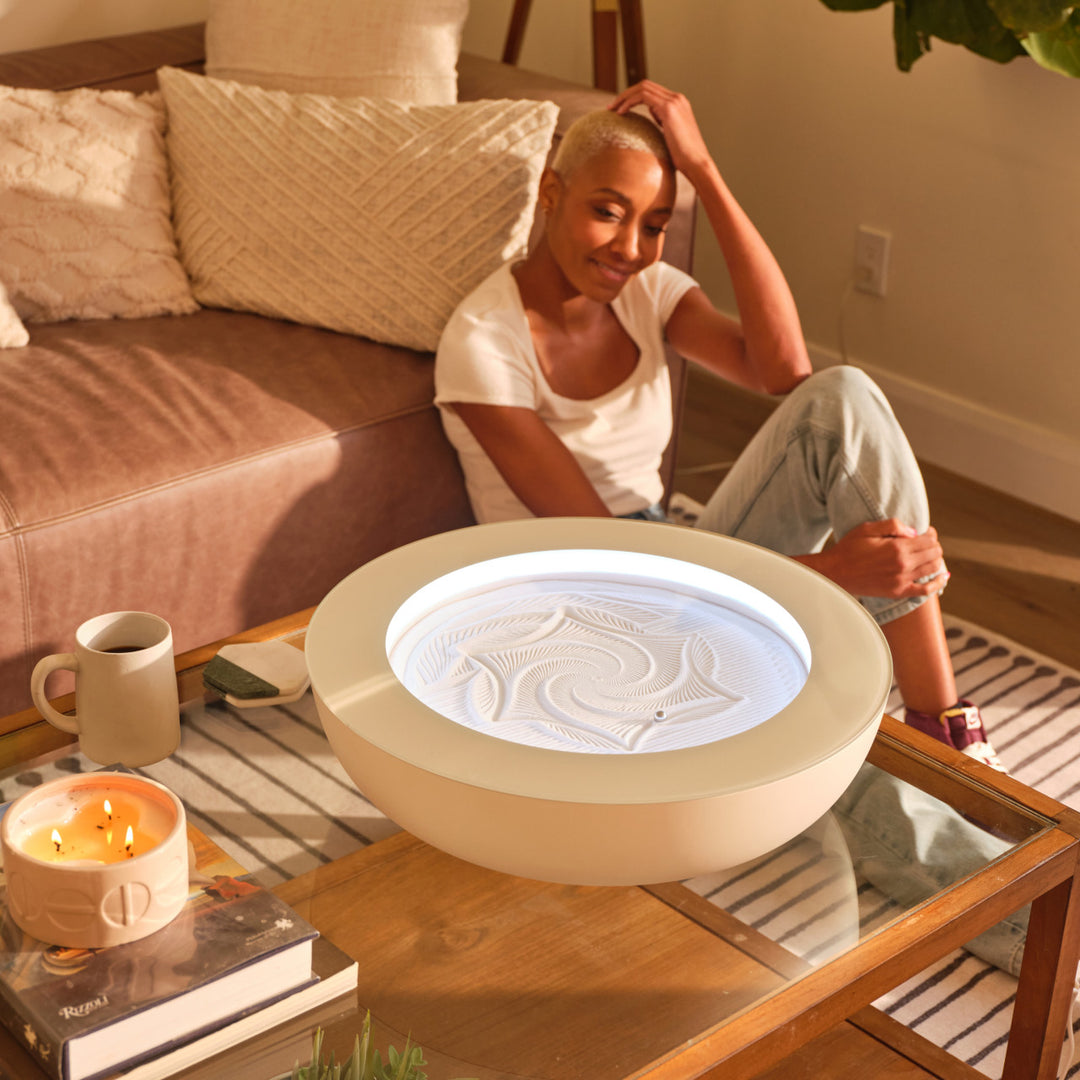 Cream | woman sits on floor practicing mindful meditation as she gazes into the drift sandscape sand table on the coffee table