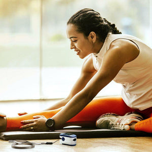Woman stretches on floor next to the Homedics Pulse Oximeter