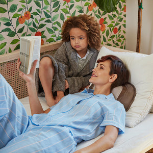 Woman reads book with child while laying on bed and enjoying neck massage from the Homedics Shiatsu Elite 3D Shiatsu and Vibration Massage Pillow with Heat