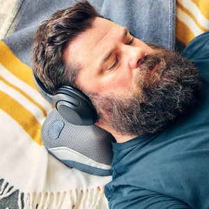 Man wearing headphones lays down and enjoys a neck massage with the Homedics Gentle Touch Gel Cordless Massager with Heat