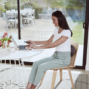 Woman sits in chair and types on laptop while enjoying the Homedics Lumbar Lift Lower Back Stretcher and Massager positioned on her lower back