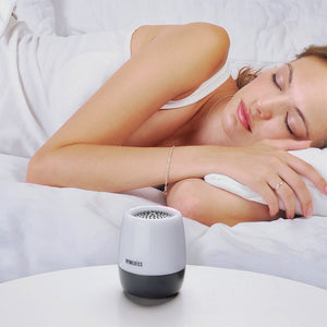 Homedics SoundSpa Traveler White Noise Sound Machine sitting on end table as woman sleeps in bed in the background