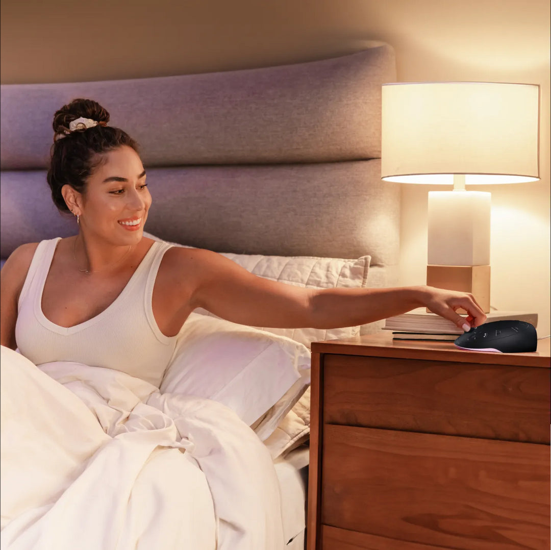Night | Homedics Portable Sound Machine with Light placed on a bedside table, while a woman relaxes in bed.