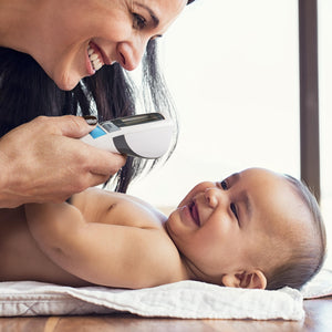 Close-up of woman smiling close to laying baby while holding the Homedics Non-Contact Infrared Thermometer