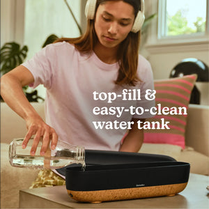A woman listens to music and adds more water to the Fireside Ultrasonic Humidifier