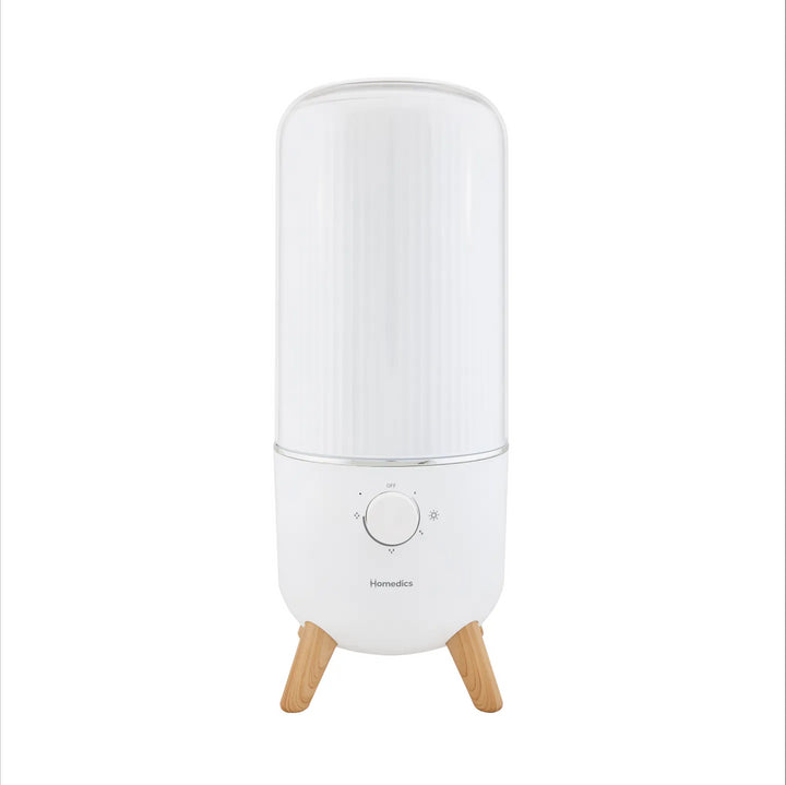 Woman reading magazines in her living room with the  Homedics® Ultrasonic Humidifier on a table next to her