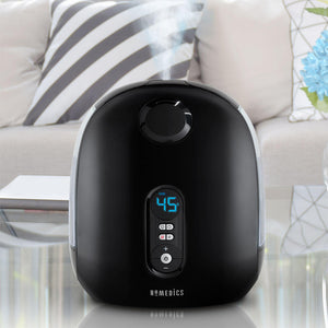 Homedics TotalComfort Deluxe Ultrasonic Humidifier powered on and sitting on table in front of couch