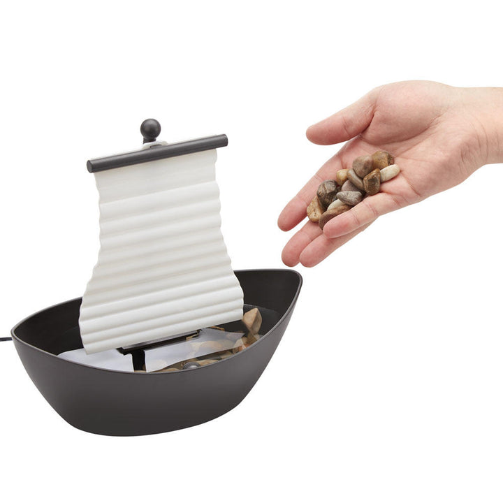 Angled view of hand adding rocks to the Homedics White Waters Relaxation Fountain