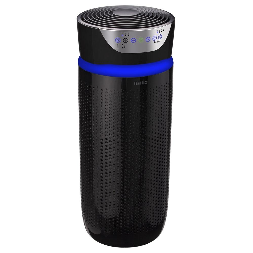 Black | Homedics TotalClean 5-in-1 UV-C Deluxe Large Room Air Purifier sits next to couch and purifies air while woman stands and checks messages on phone by the window