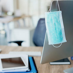 Homedics Single Use Ear-Loop Face Mask dangles on the edge of a computer monitor in office