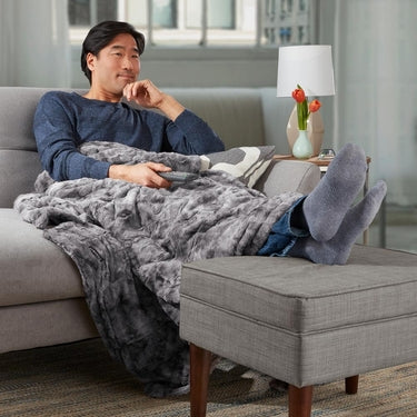 Man relaxes on chair while covered with the Homedics Cordless Throw & Cape with Soothing Heat & Vibrating Massage