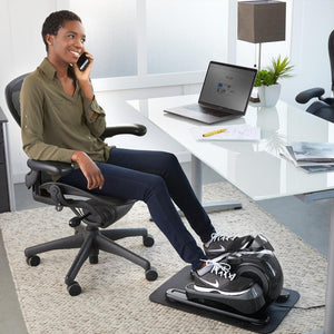 Woman sits in chair in office with feet on the Homedics Stayfit Mini-Stepper