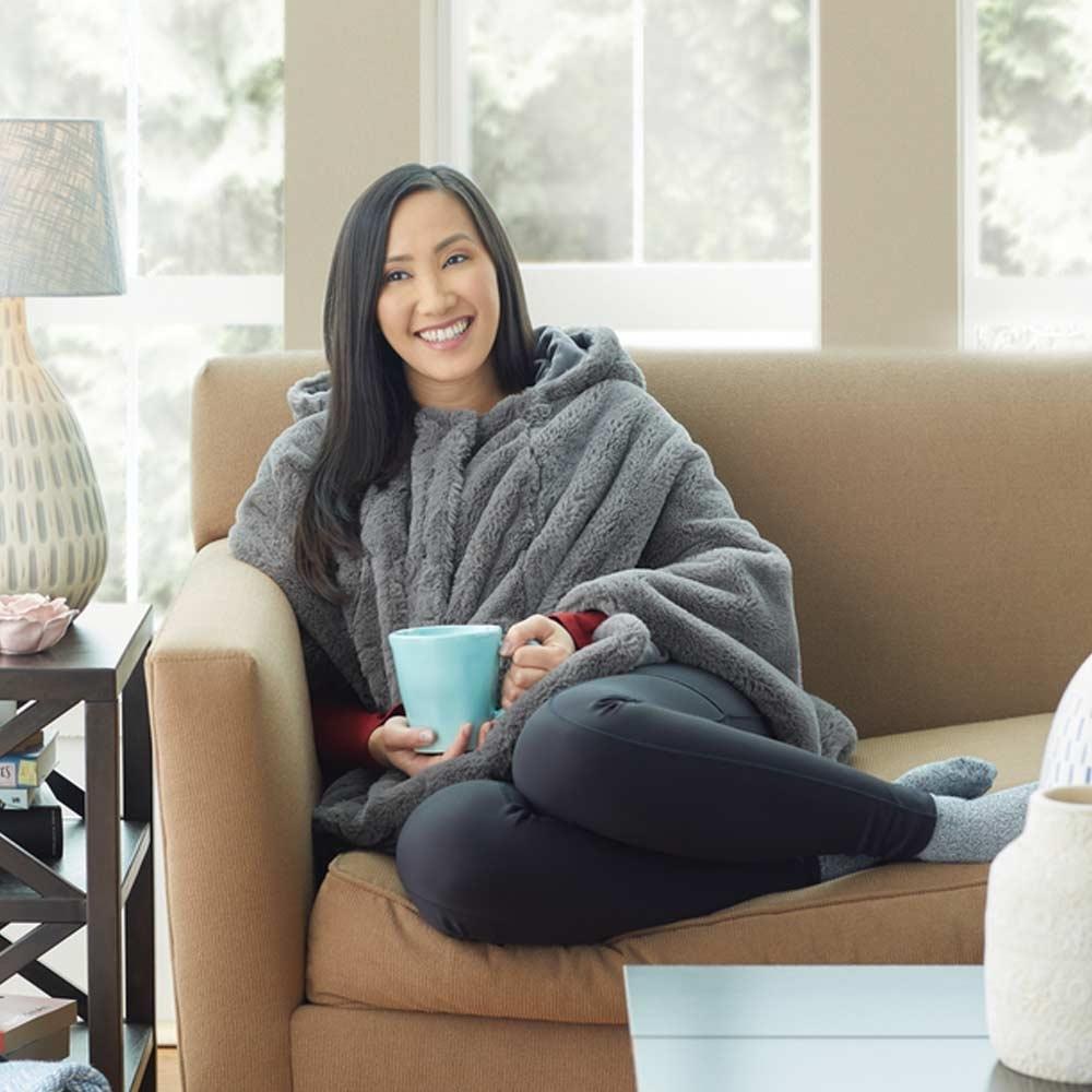 Woman relaxes on couch while wearing the Homedics Cordless Massaging Cape with Vibration and Soothing Heat