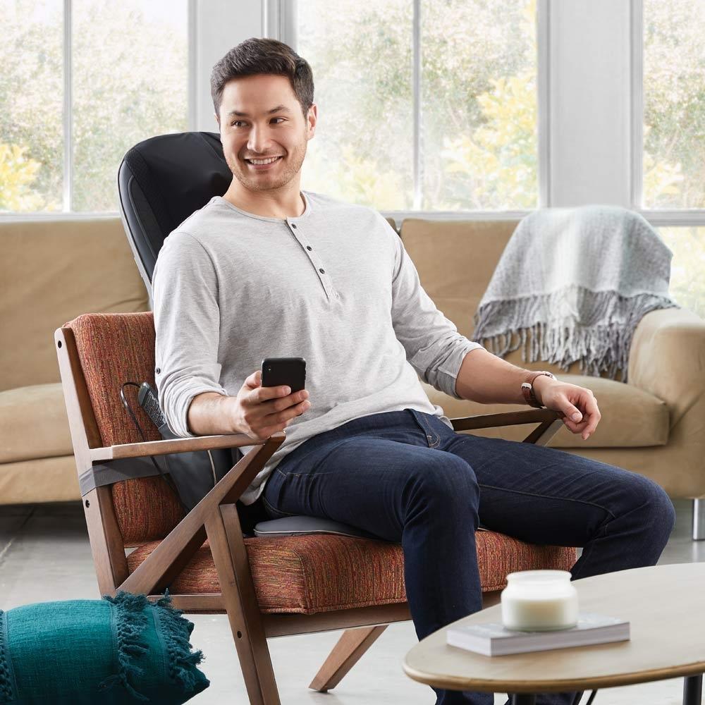 Man sitting on chair enjoys a massage from the Homedics Serenity Shiatsu Massage Cushion with Sound and Meditation