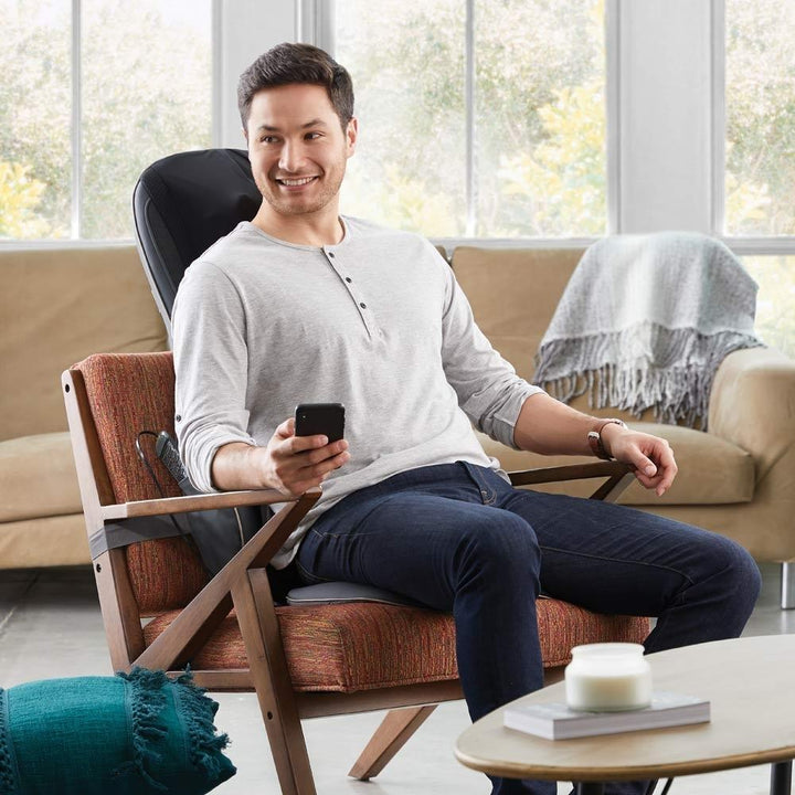 Man sitting on chair enjoys a massage from the Homedics Serenity Shiatsu Massage Cushion with Sound and Meditation