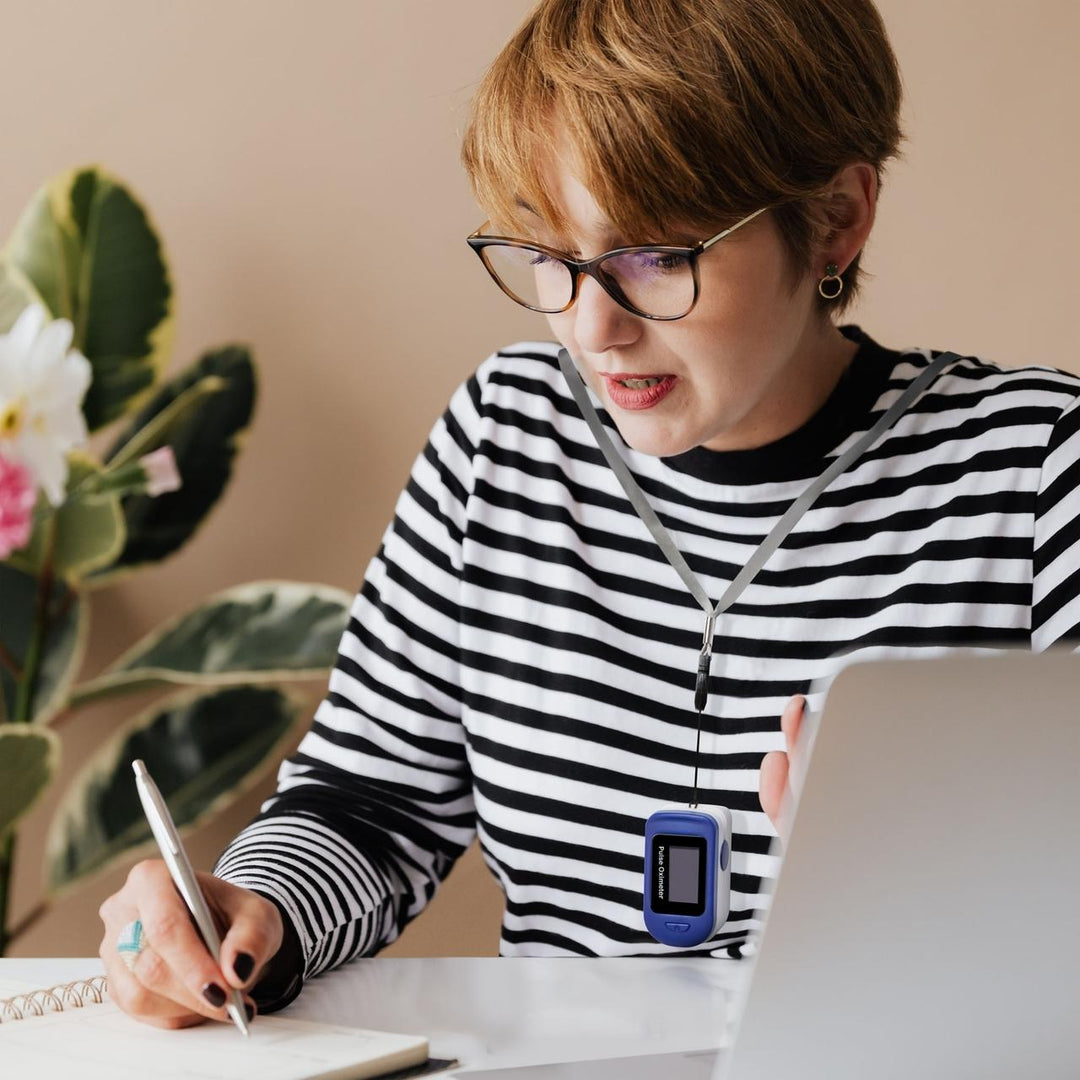 Woman works at office desk while wearing Homedics ACCARE Pulse Oximeter around neck