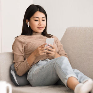 Young woman relaxes on couch while enjoying a lower back massage from theHomedics Gentle Touch Gel Cordless Massager with Heat