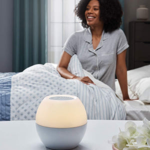 Woman sits up in bed next to her Homedics SoundSpa Sunrise with orange lighting