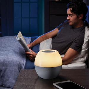 Man sits up in bed next to his Homedics SoundSpa Sunrise with orange lighting