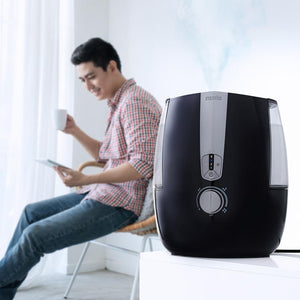 Man sits in chair looking at tablet with the Homedics TotalComfort Plus Ultrasonic Humidifier in the foreground