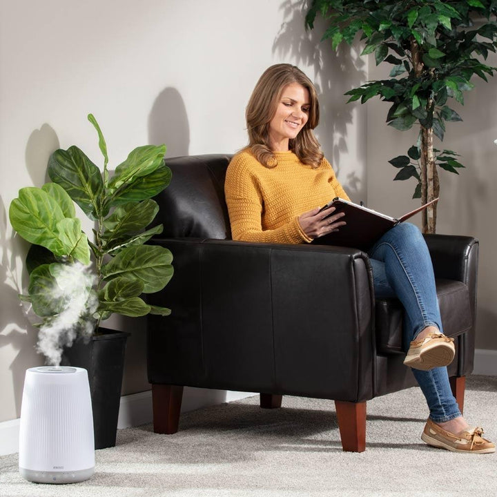 Woman sits in chair next to the Homedics TotalComfort Ultrasonic Humidifier