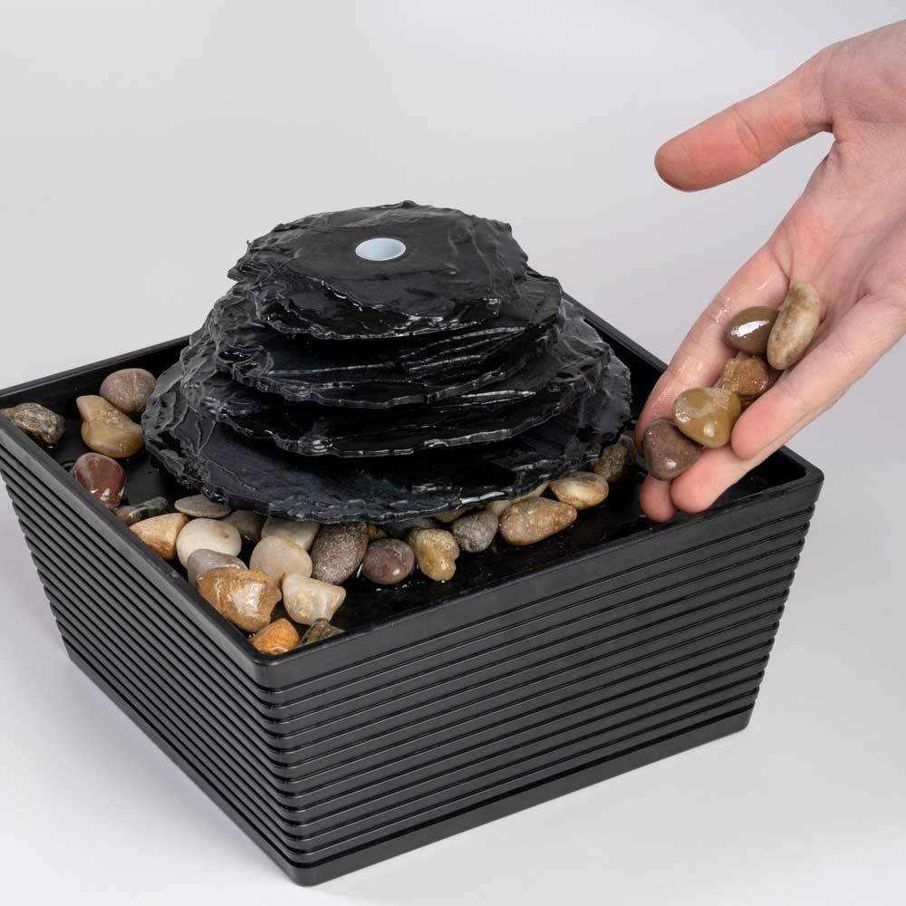 Hand adds rocks to the Homedics Envirascape Entrance Tabletop Relaxation Fountain