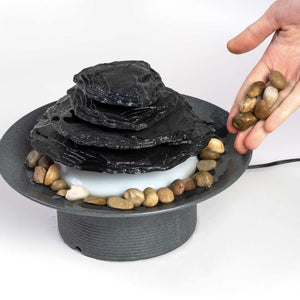 Angled view of hands adding rocks to the Mirra Zen Gray Tabletop Relaxation Fountain